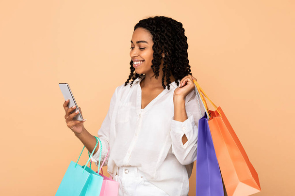 Felice ragazza nera utilizzando Smartphone Holding Shopper Borse, Studio Shot - Foto, immagini