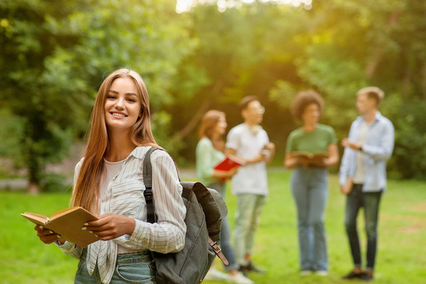 Feliz sorrindo estudante menina segurando livro posando ao ar livre no campus universitário
 - Foto, Imagem