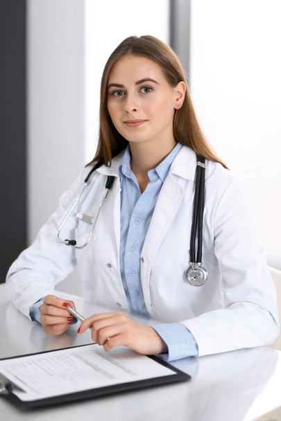 Doctor woman filling up medical form while sitting at the desk in hospital office. Physician at work. Medicine and health care concept - Foto, Imagen