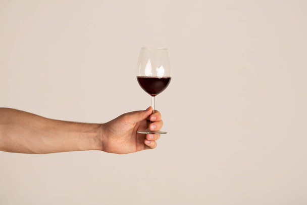 Male hand holding glass of red wine on light background, closeup with copy space - Φωτογραφία, εικόνα