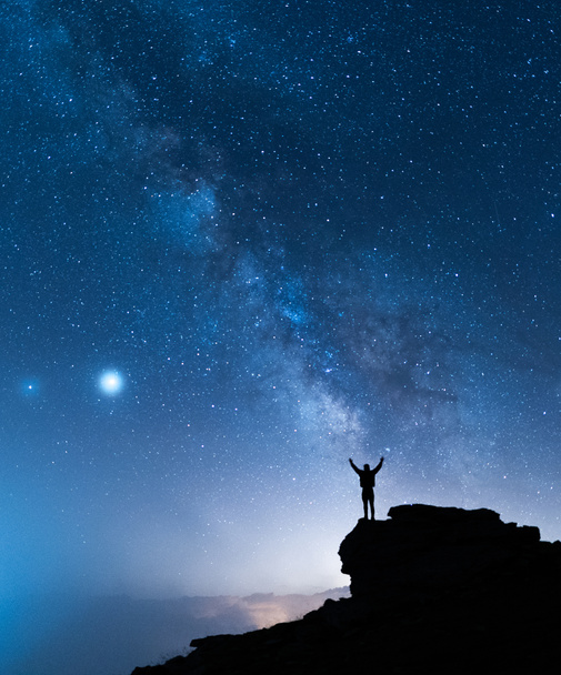 O Homem e o Universo. Uma pessoa está em pé no topo da colina ao lado da Via Láctea com as mãos levantadas para o ar
. - Foto, Imagem