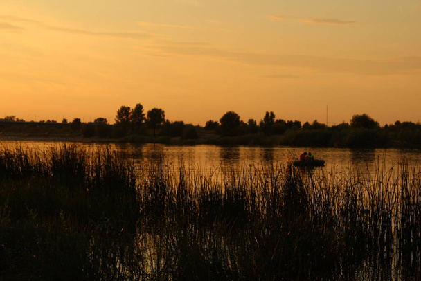вечерний ночной пейзаж у реки оранжевый желтый розовый закат дикие утки плавают возле берега вы можете увидеть напротив берега моста деревьев - Фото, изображение