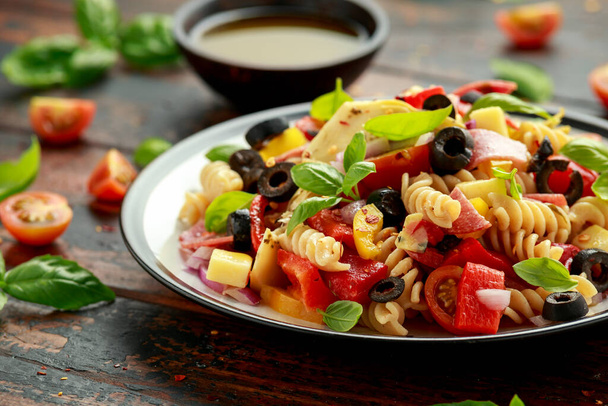 Antipasto salad with pasta, tomato, olives, red onion, bell pepper, salami, cheese, artichoke and basil. - Foto, Bild