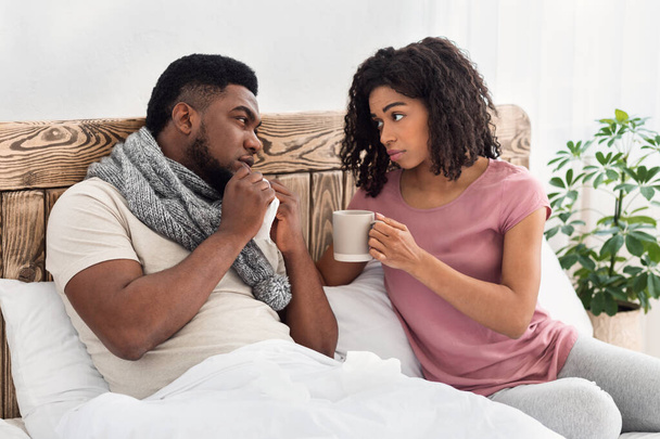 Atenta esposa negra dando a su marido enfermo bebida caliente - Foto, imagen
