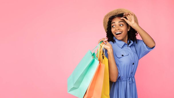 Emocionada chica africana llevando bolsas de compras mirando a un lado, fondo rosa - Foto, imagen