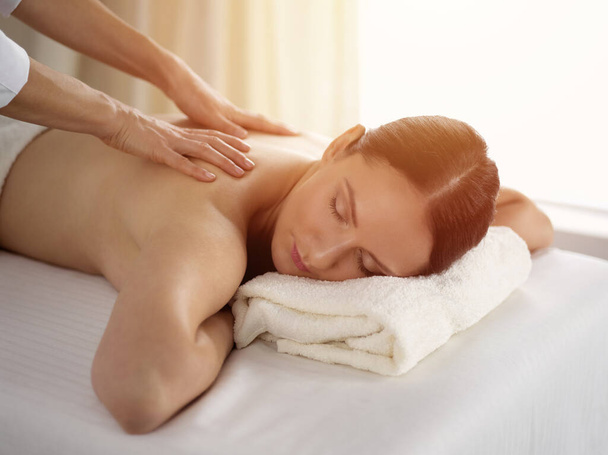 Mujer morena bonita disfrutando del procedimiento de masaje de espalda en el salón de spa soleado. Concepto de belleza - Foto, Imagen
