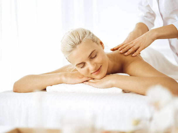 Beautiful blonde woman enjoying back massage with closed eyes. Spa salon concept - 写真・画像