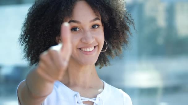 Happy cheerful African-American girl with Afro, toothy smile, shows her thumbs up, gesture of well being and approval, good quality. Positive emotions body language beautiful young woman said Yes.  - Footage, Video