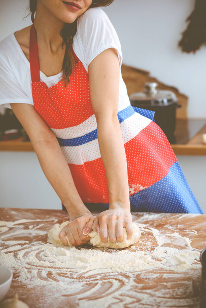 Young brunette woman cooking pizza or handmade pasta in the kitchen. Housewife preparing dough on wooden table. Dieting, food and health concept - Foto, afbeelding