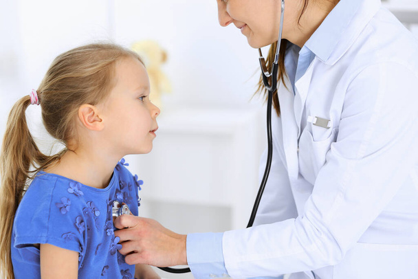 Doctor examining a little girl by stethoscope. Happy smiling child patient at usual medical inspection. Medicine and healthcare concepts - Photo, image