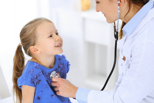 Doctor examining a little girl by stethoscope. Happy smiling child patient at usual medical inspection. Medicine and healthcare concepts - Фото, изображение
