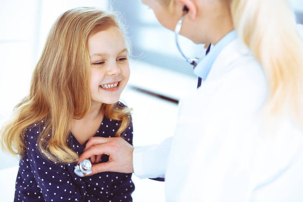 Врач осматривает ребенка стетоскопом. Милая малышка на приеме у врача. Концепция медицины. Тонированное фото - Фото, изображение