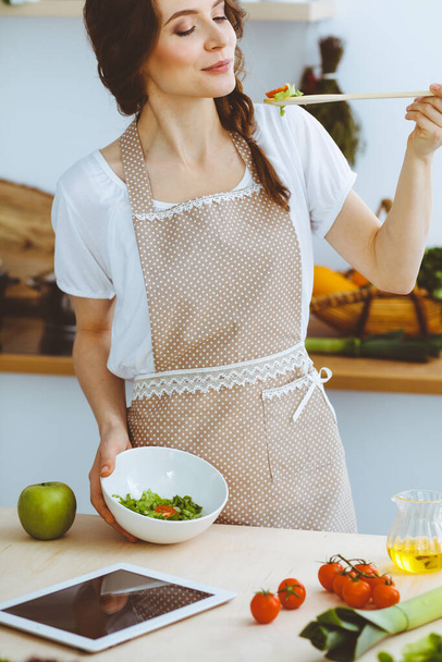Young brunette woman cooking in kitchen. Housewife holding wooden spoon in her hand. Food and health concept - Photo, Image