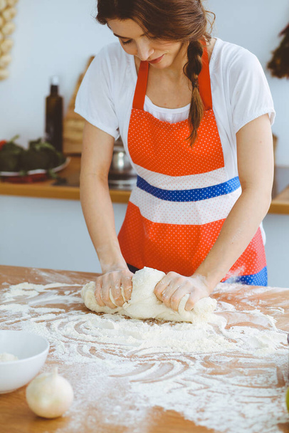 Young brunette woman cooking pizza or handmade pasta in the kitchen. Housewife preparing dough on wooden table. Dieting, food and health concept - Foto, Imagem