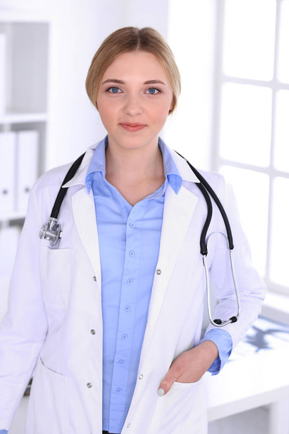 Young woman doctor at work in hospital looking at camera. Blue colored blouse of therapist looks good. Medicine and healthcare concept - Photo, Image
