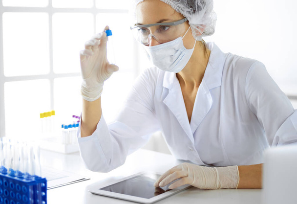 Professional female scientist in protective eyeglasses researching tube with reagents in laboratory. Concepts of medicine and research - Foto, imagen
