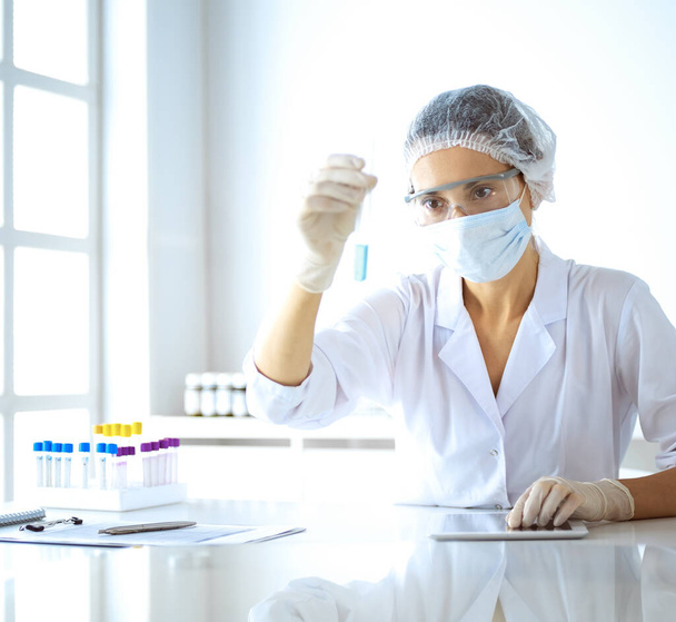 Professional female scientist in protective eyeglasses researching tube with reagents in laboratory. Concepts of medicine and research - Фото, изображение