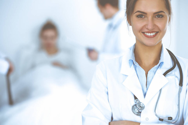 Doctora sonriendo en el fondo con paciente en la cama y dos doctores - Foto, Imagen