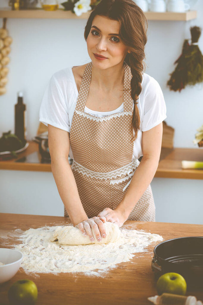 Young brunette woman cooking pizza or handmade pasta in the kitchen. Housewife preparing dough on wooden table. Dieting, food and health concept - Foto, Bild