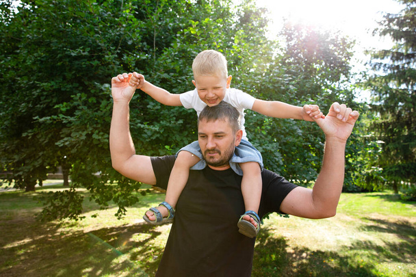Father holds his son on his back like an airplane in park outdoor. Father plaing with son. Kindred love. Affection. Trusting relationship - Fotografie, Obrázek