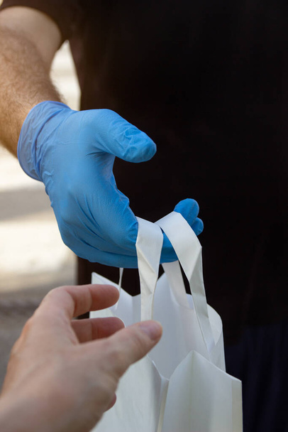 Auslieferer in Schutzmaske und Handschuhen mit einer Papiertüte. Lieferservice unter Quarantäne, Krankheitsausbruch, Covid-19-Coronavirus-Pandemie - Foto, Bild