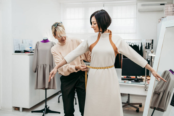 Professionele ontwerper werkt aan nieuwe trendy jurk met vrouwelijk model in de modestudio. Creatieve mensen concept. - Foto, afbeelding