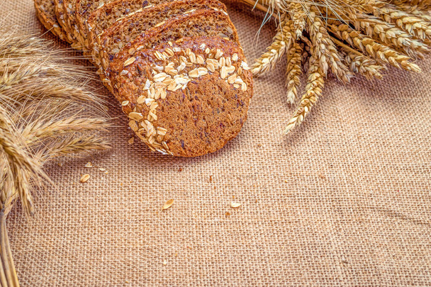 Ψωμί μπαγκέτας. Ψωμί σίκαλης με τραγανά καρβέλια και ψίχουλα. Φρέσκο καρβέλι χωριάτικο παραδοσιακό ψωμί με στάρι σταριού στο αυτί ή φυτό ακίδα σε φυσικό βαμβακερό φόντο. Concept - Μαγειρική στο σπίτι - Φωτογραφία, εικόνα