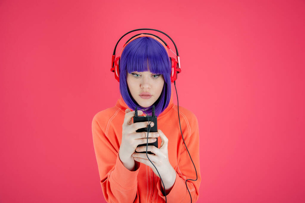 Portrait funky beautiful young woman with blue hair in hoodie on bright pink background. Alternative girl with headphone listens cool music in her smartphone. Unusual youth fashion concept. Hot image. - Fotoğraf, Görsel