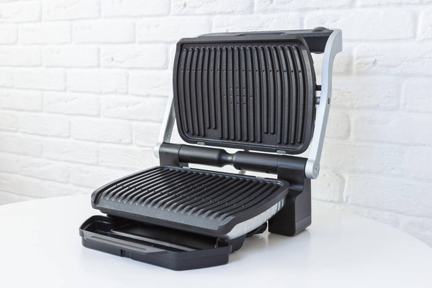 Open empty electric grill. Barbecue for home use on white kitchen background. - Фото, изображение