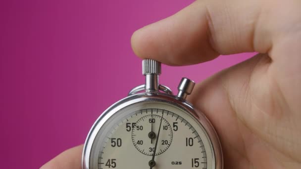 Κοντινό αναλογικό χρονόμετρο σε mans χέρι σε ροζ φόντο αρχίζει και σταματά - Πλάνα, βίντεο