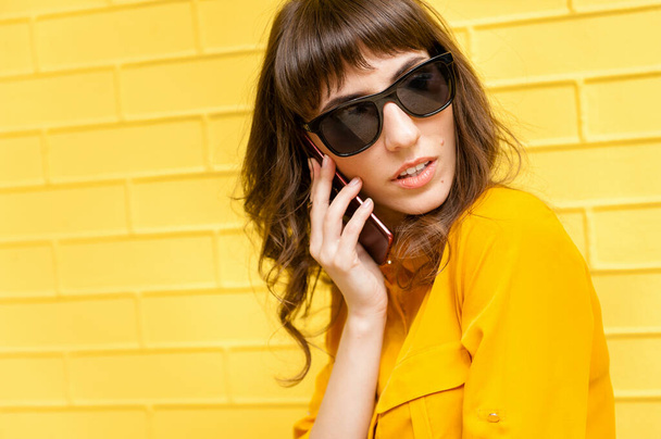 Портрет дівчини в жовтій булочці на жовтій стіні. Девушка розмовляє по телефону і озирається. - Фото, зображення