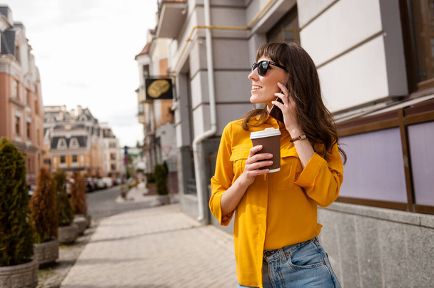 Молода дівчина розмовляє по телефону з чашкою кави в руці
 - Фото, зображення