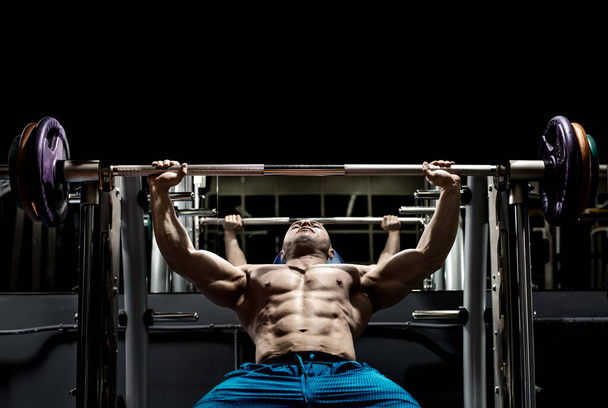 Man bodybuilder perform exercise barbell bench press in GYM lying on back. Empty black space for text - 写真・画像