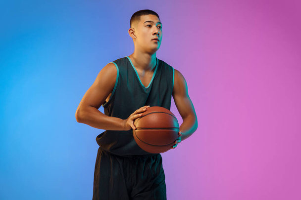 Young basketball player in motion on gradient studio background in neon light - Fotografie, Obrázek
