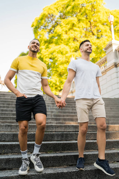Portrait of happy gay couple spending time together and holding hands while walking in the street. Lgbt and love concept. - Foto, Imagen