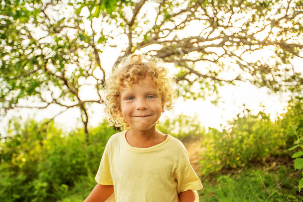 Portré egy göndör fehér fiúról a parkban naplementekor - Fotó, kép