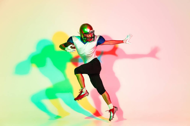 American football player isolated on gradient studio background in neon light with shadows - Foto, immagini