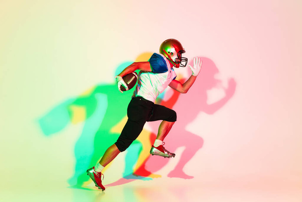 American football player isolated on gradient studio background in neon light with shadows - Фото, изображение