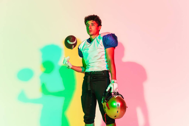 American football player isolated on gradient studio background in neon light with shadows - Фото, зображення