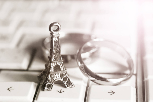Uma estátua da Torre Eiffel e anéis de casamento no teclado do laptop, tonificado
 - Foto, Imagem