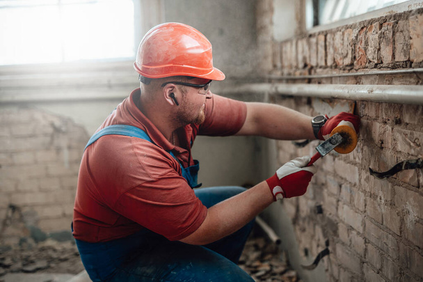 Builder on a construction site working on a brick wall with a hammer - Фото, изображение