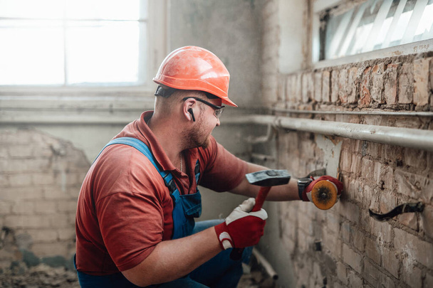 Constructeur travailleur sur un chantier de construction travaillant sur un mur de briques avec un marteau - Photo, image
