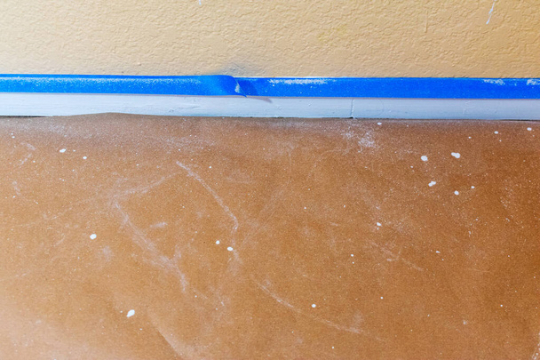 Cinta azul para pintores junto al revestimiento de la pared y el suelo protegida con papel de construcción marrón contra derrames, goteos de pintura y salpicaduras, durante una renovación y pintura del hogar. - Foto, Imagen
