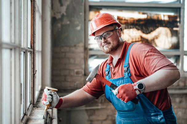 Constructor de confianza en un sitio de construcción que trabaja en una pared de ladrillo con un martillo - Foto, Imagen