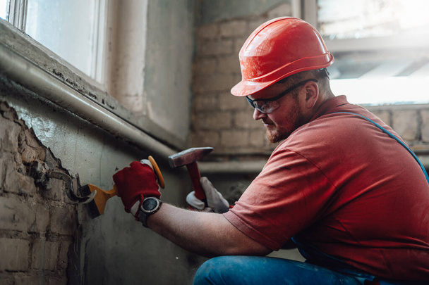 Constructeur sur un chantier de construction travaillant sur un mur de briques avec un marteau - Photo, image