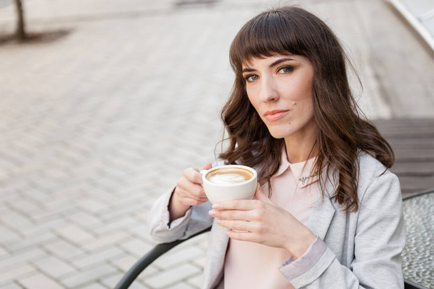 Chica con una taza de café se sienta en un café y mirando a la cámara
 - Foto, imagen