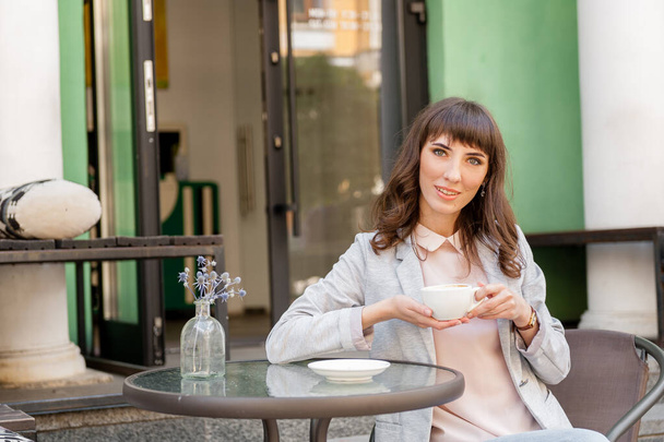 κορίτσι σε ένα καφέ στο δρόμο κάθεται και πίνει καφέ - Φωτογραφία, εικόνα