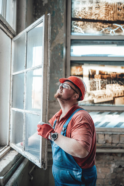 Builder working with a window at a construction site - Photo, Image