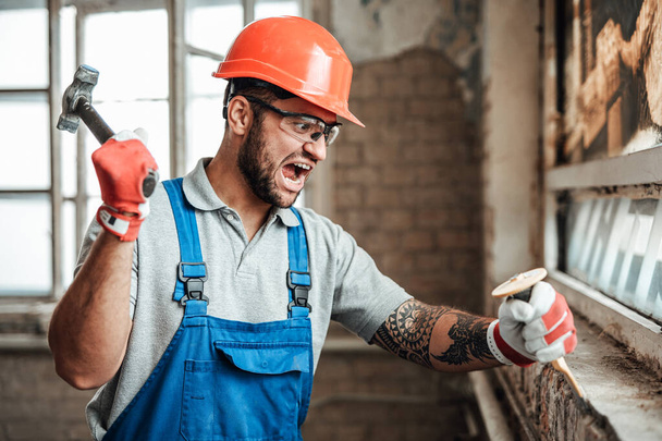 Carried away by work funny contractor strikes with a hammer, screaming - Foto, Bild