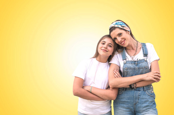 Young woman with teenage girl smiling and looking at camera. Cheerful teenage daughter with young mom on a yellow background - 写真・画像